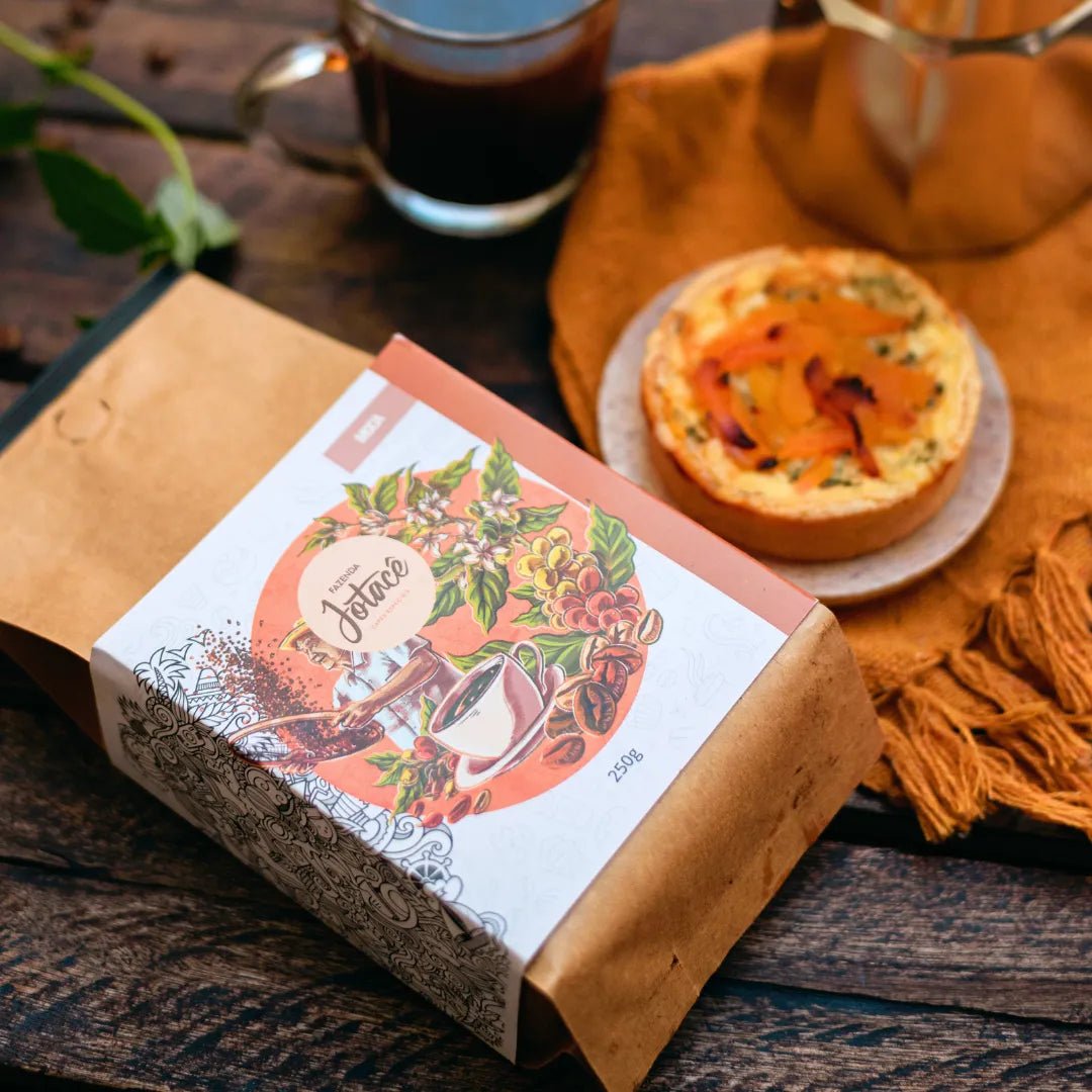 Café Microlote Moca ao lado de um quiche e uma xícara de café sobre mesa rústica de madeira