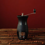 Moedor Manual Black de Café da Mimo Style com grãos de café ao redor sobre mesa de madeira.