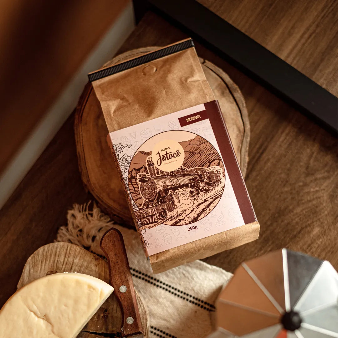 Embalagem de Café Jotacê Mogiana com acessórios de café e queijo em mesa de madeira