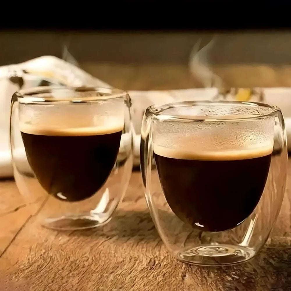 Duas xícaras de café expresso em copos de vidro duplo sobre uma superfície de madeira.
