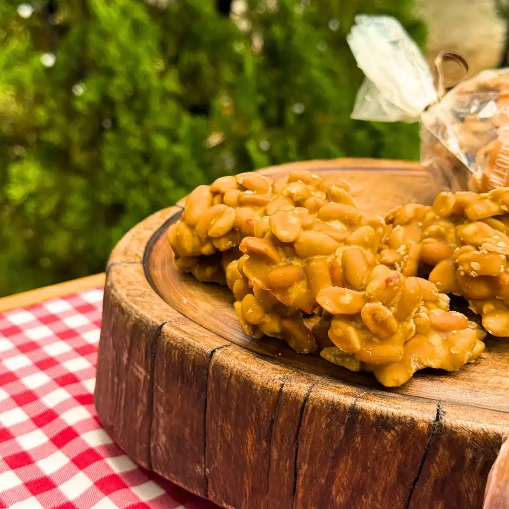 Pedaços de pé de moleque com rapadura artesanal sobre tábua de madeira rústica, mostrando amendoins inteiros caramelizados na rapadura crocante, pacote ao fundo desfocado