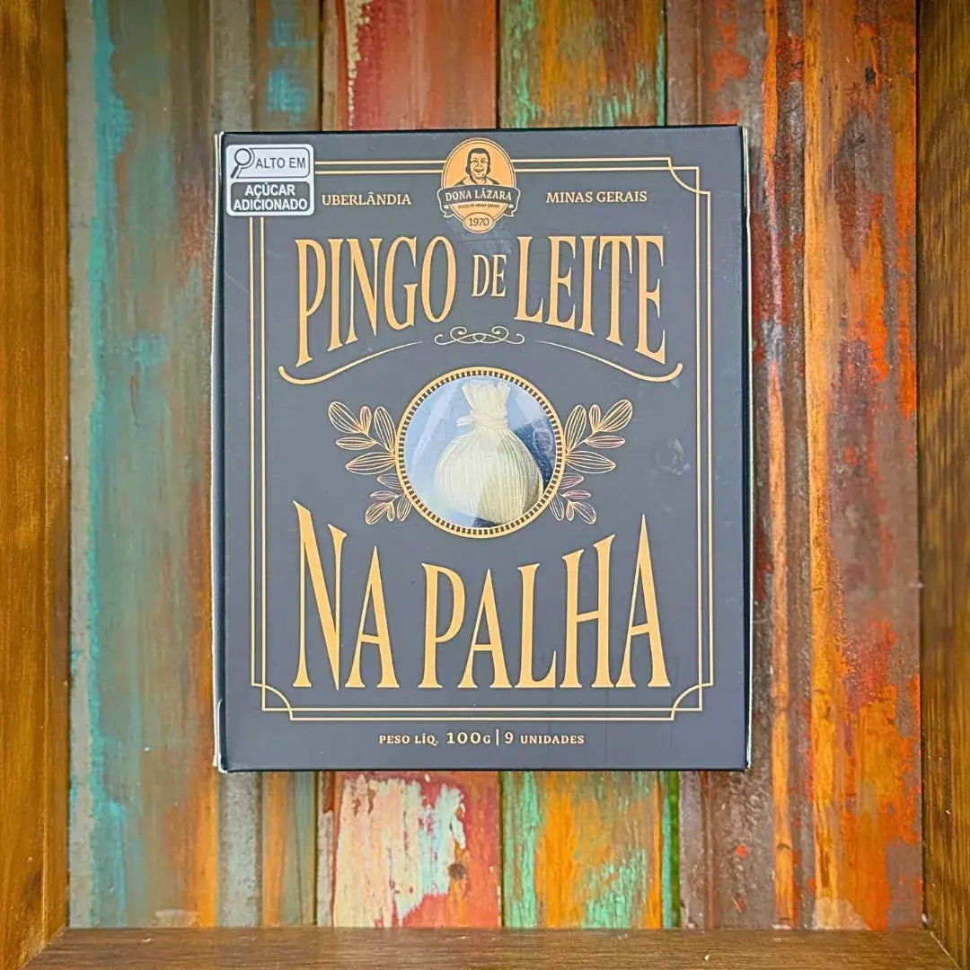 Caixa azul-escuro e dourada de Pingo de Leite na Palha Dona Lázara 100g sobre parede de madeira colorida, design elegante com visor circular e tipografia vintage
