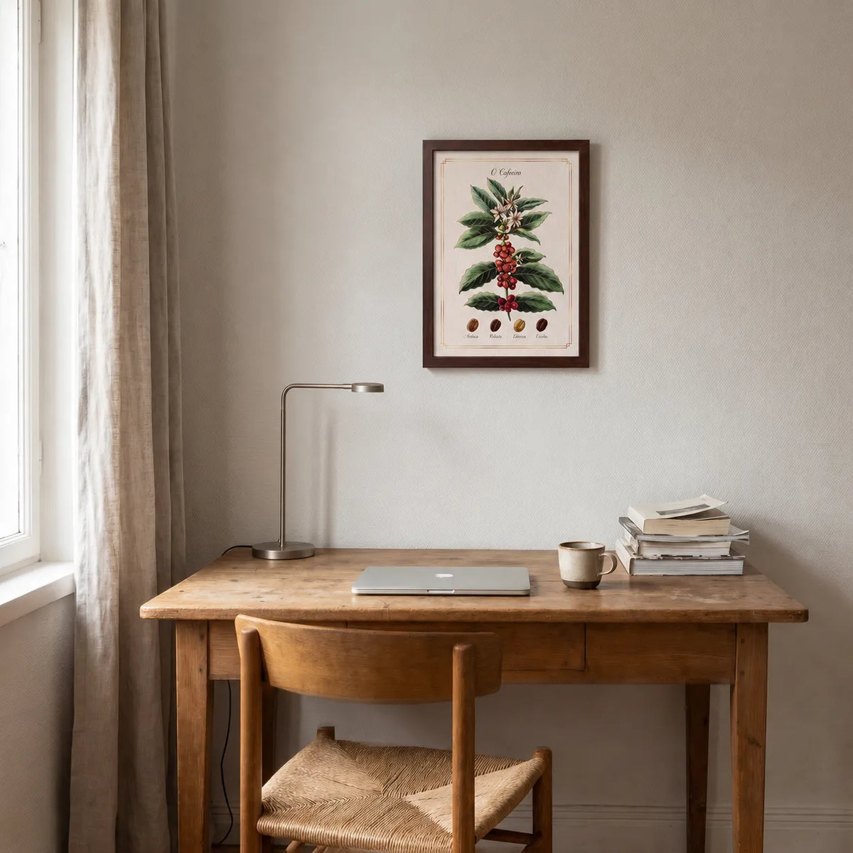Quadro botânico "O Cafeeiro" com moldura de madeira escura na parede de um cantinho de trabalho, acima de escrivaninha rústica com luminária, notebook, caneca de cerâmica e pilha de livros.