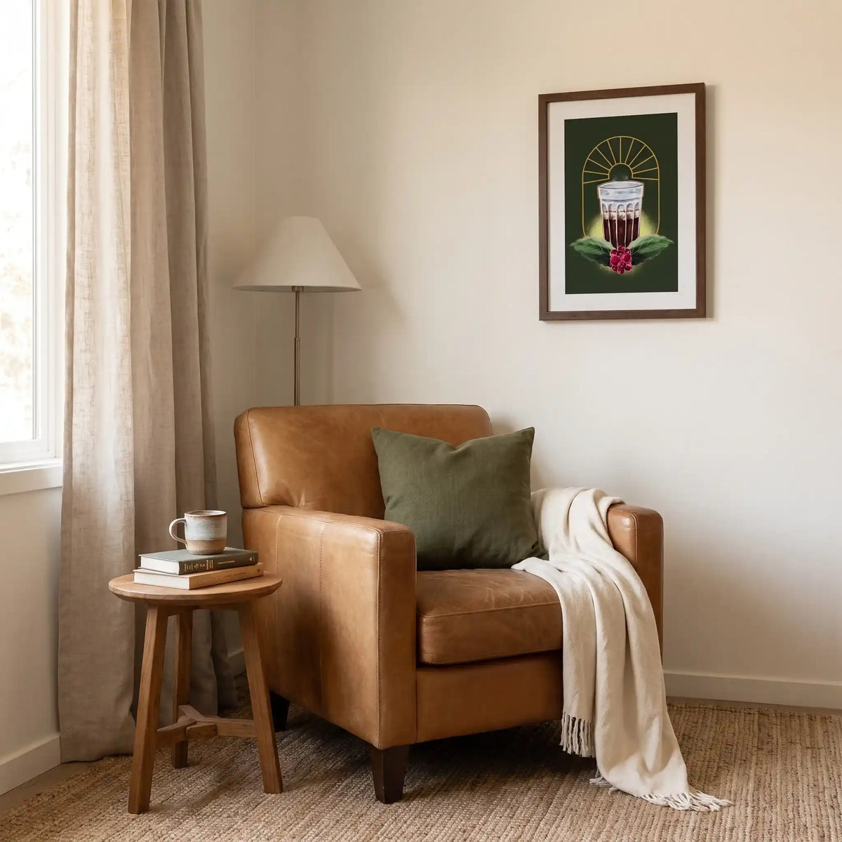 Quadro do café com moldura de madeira escura na parede de um canto de leitura, acima de poltrona de couro caramelo com almofada verde, manta creme e mesinha lateral com livros e caneca.