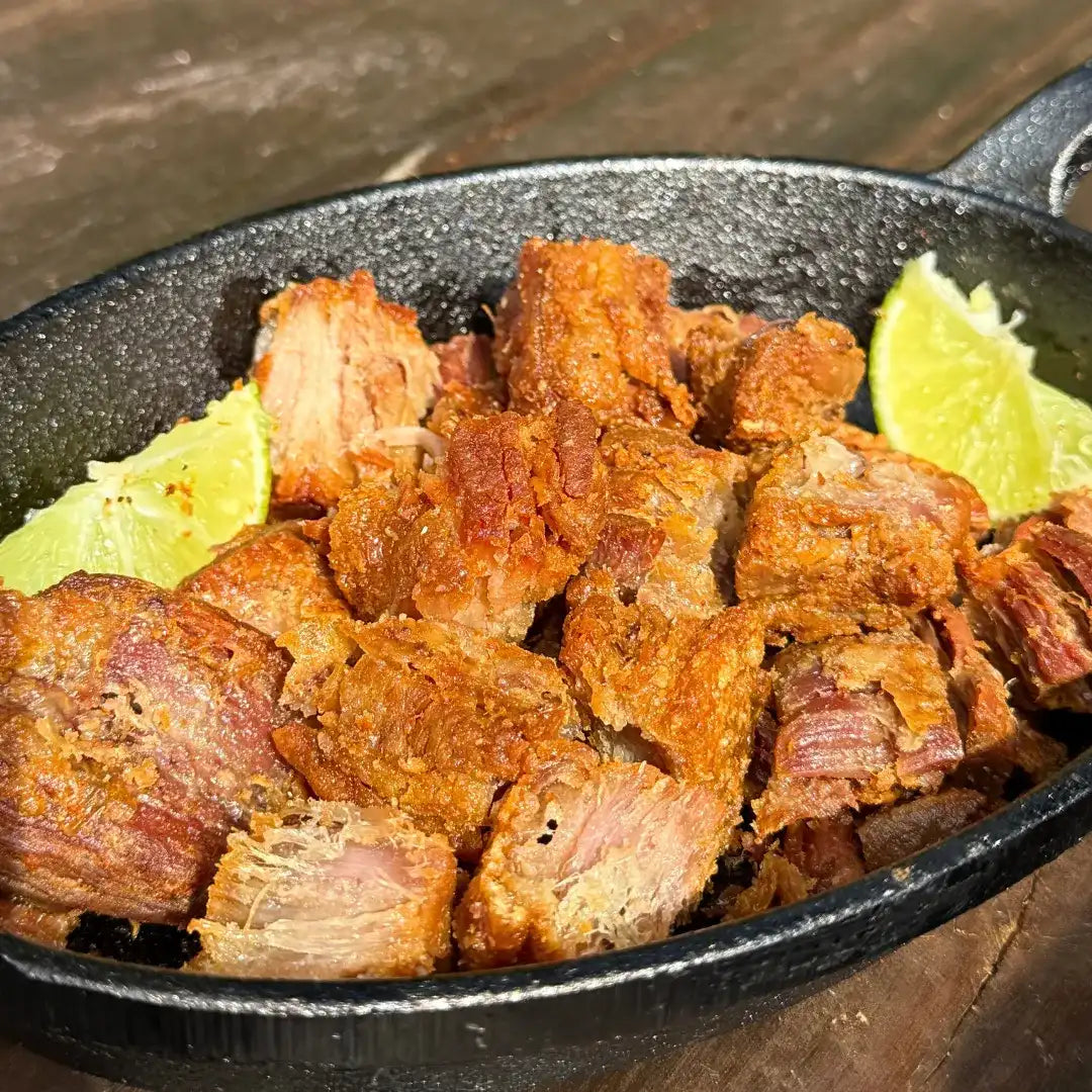 Close de torresmo Xavante pururucado e dourado em panela de ferro, com gomos de limão ao lado, mostrando a casquinha crocante da carne de lata mineira.