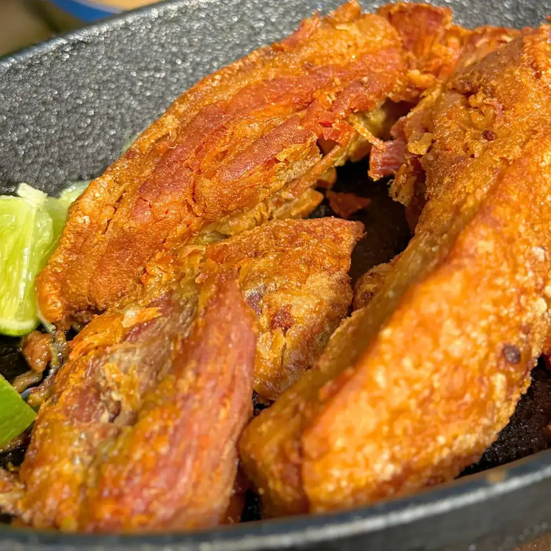 Pedaços de Torresmo Especial Xavante 900g servidos em frigideira de ferro com limão, prontos pra comer, com a casquinha dourada característica.