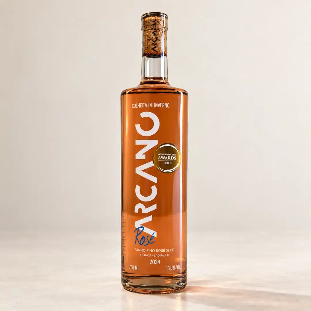 Garrafa do vinho rosé seco Arcano Syrah 750ml de frente, em fundo claro, com rótulo vertical branco, rolha à vista no gargalo e selo de ouro do Wines of Brazil Awards.