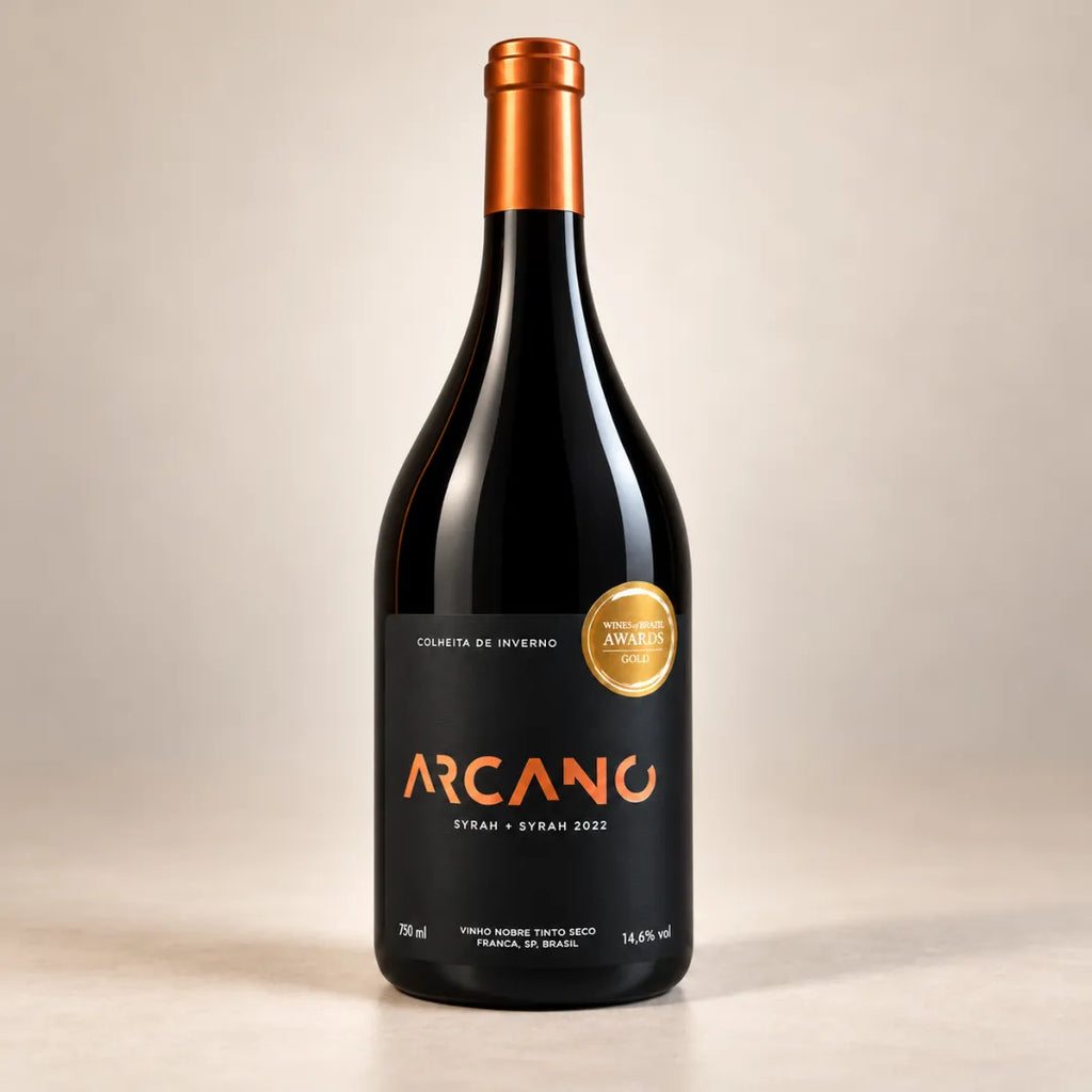 Garrafa do vinho Syrah Arcano 750ml de frente, em fundo claro, com rótulo preto Syrah + Syrah 2022, cápsula cobre e selo de ouro do Wines of Brazil Awards.