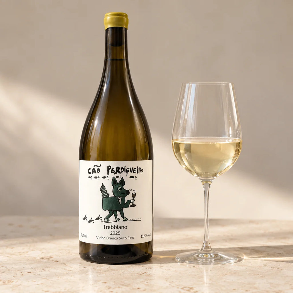 Vinho trebbiano Cão Perdigueiro ao lado de uma taça de vinho branco servida, com luz de fim de tarde