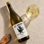 Vinho de uva trebbiano Cão Perdigueiro deitado ao lado de uma taça, visto de cima, com a pata de um cachorro