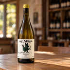 Garrafa de vinho branco brasileiro Cão Perdigueiro Trebbiano sobre mesa de madeira, com prateleiras de adega ao fundo